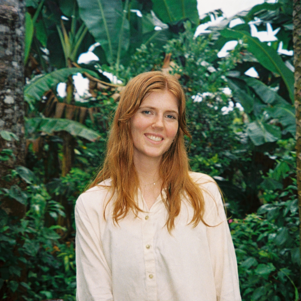 Smiling woman in lush green outdoor setting.