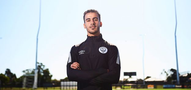 Footballer in black tracksuit standing on field.