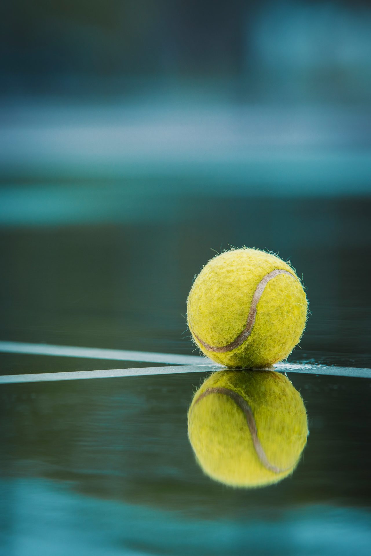 Yellow tennis ball reflecting on wet court.