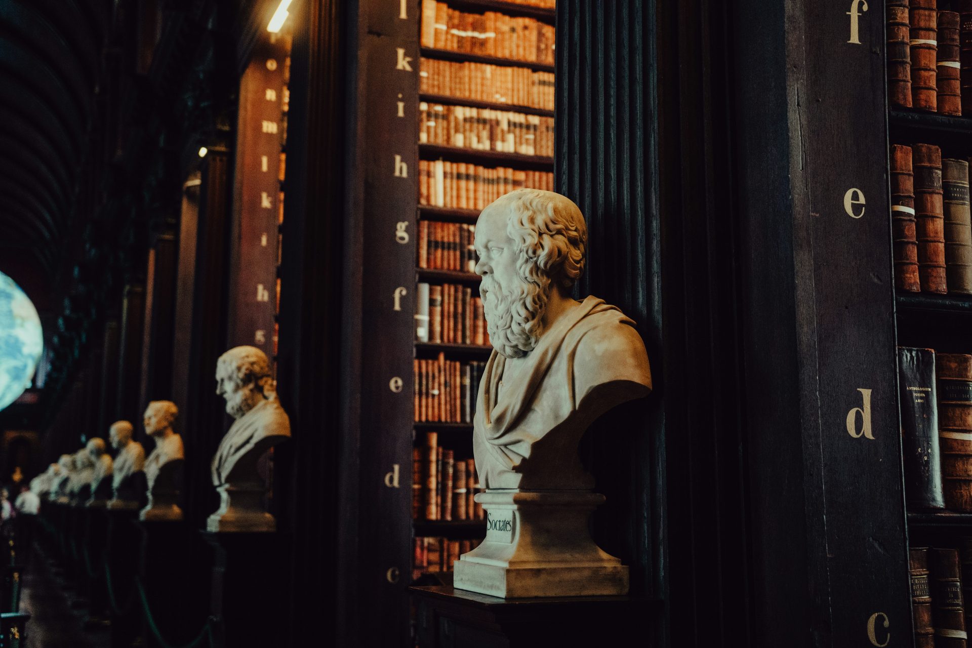 Marble bust in historic library with bookshelves.